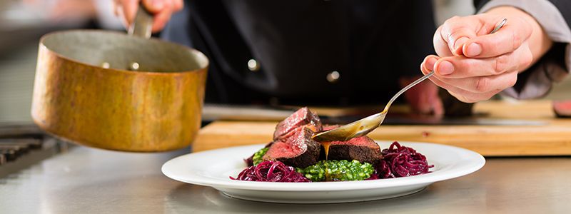 Kock som lägger upp mat på tallrik på kryssning.